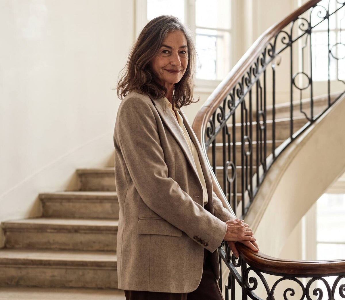 Femme en blazer beige appuyée à la rampe d'un escalier haussmannien
