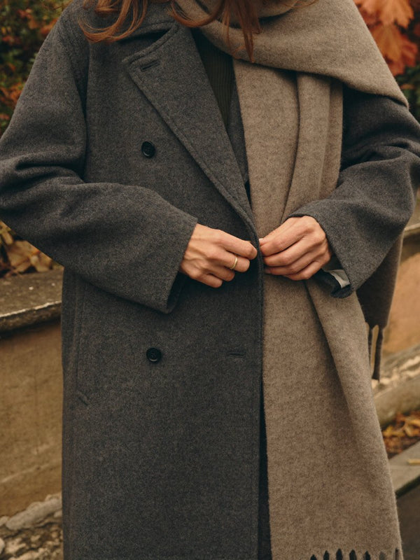 Mains boutonnant un long manteau gris avec une écharpe taupe