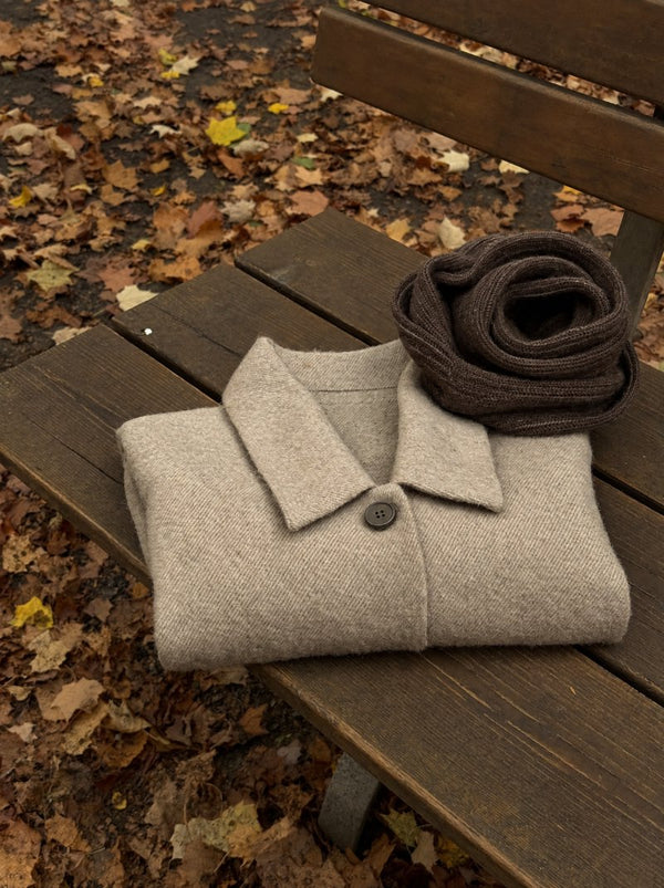 Manteau en laine beige et écharpe marron posés sur un banc parmi les feuilles d'automne