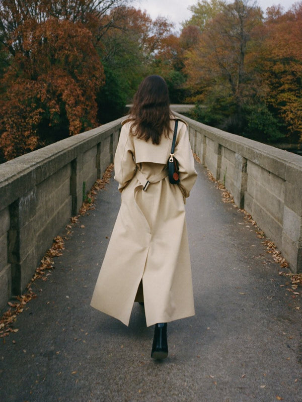 Femme en trench beige de dos sur un pont en pierre en automne