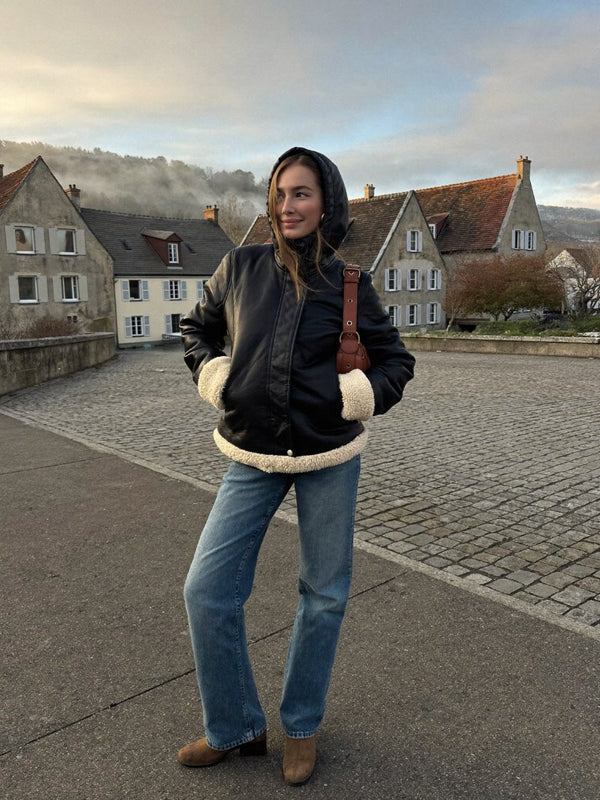 Femme en veste à capuche doublée sherpa noire sur une place de village en automne